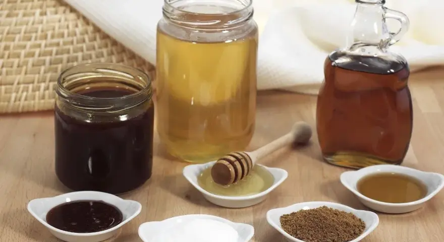 Domowy syrop cukrowy i kupny syrop barmański obok miodu i cukru.