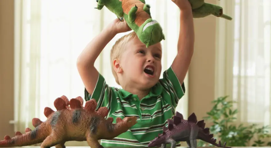 4 letnie dziecko bawi się pluszowymi dinozaurami, wyobrażając sobie prehistoryczną przygodę.