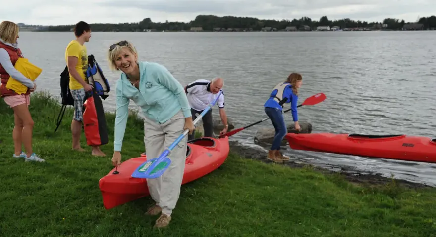 Familie bereitet sich auf einen Aktivurlaub an der Ostsee vor, holt Kajaks und Paddel aus dem Wasser.