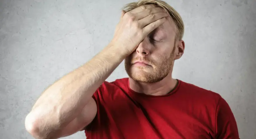 Uomo con mano sulla fronte, occhi chiusi, espressione di stress. Possibili sintomi di attacchi epilettici da stress.