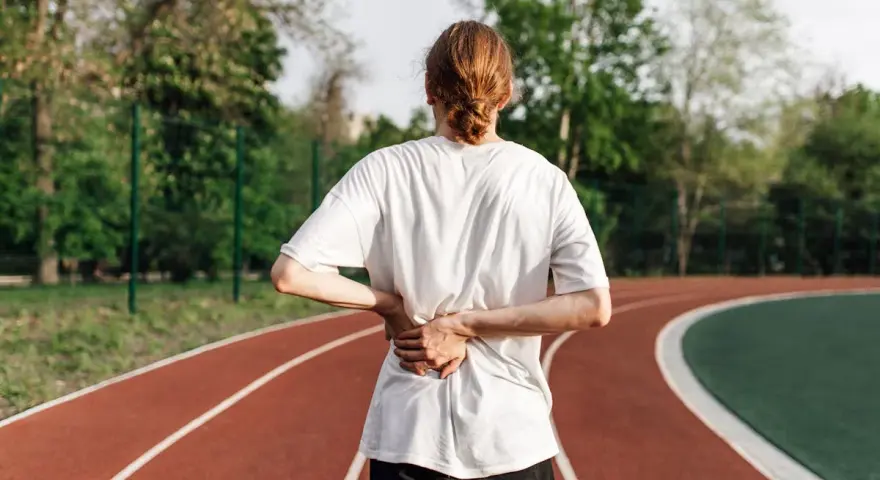 Une personne se tient sur une piste de course, le dos douloureux. La question se pose : peut-on courir avec une sciatique ?