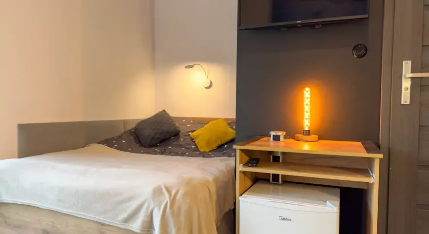 Przytulny pokój z łóżkiem, ozdobną lampą i lodówką. Idealne miejsce na **weekend w Karpaczu**.
