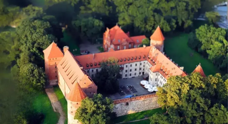 Zamek w Bytowie otoczony zielenią, z czerwonymi dachami i kamiennymi murami, wygląda jak z bajki.