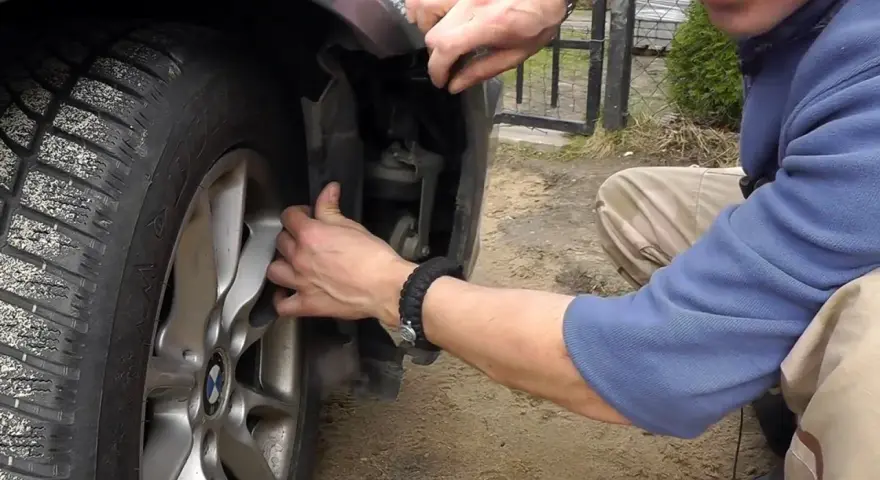 Naprawa awarii PDC BMW. Mężczyzna demontuje fragment nadkola, by dostać się do czujników parkowania.