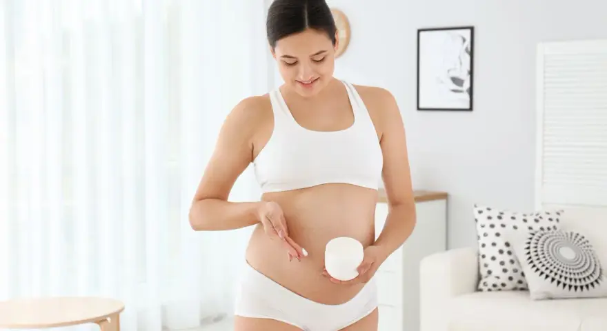 Kobieta w ciąży smaruje brzuch kremem, łagodząc swędzenie skóry.