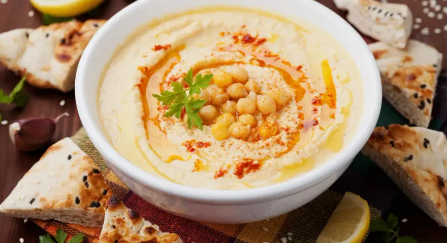 Un bol de houmous maison, garni de pois chiches, de persil et de paprika, servi avec du pain pita, du citron et de l'ail.