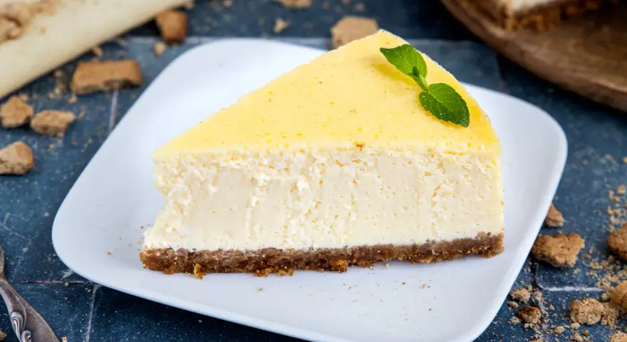 Ein cremiges Stück New York Cheesecake mit einem Keksboden, garniert mit Minze.