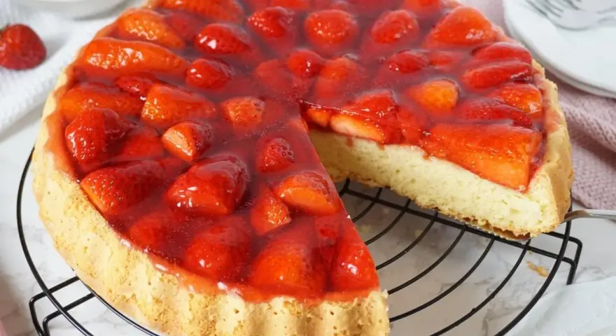Ein saftiger tortenboden mit erdbeeren, bedeckt mit glänzendem Tortenguss. Ein Stück wurde bereits entnommen, um die köstliche Füllung zu zeigen.