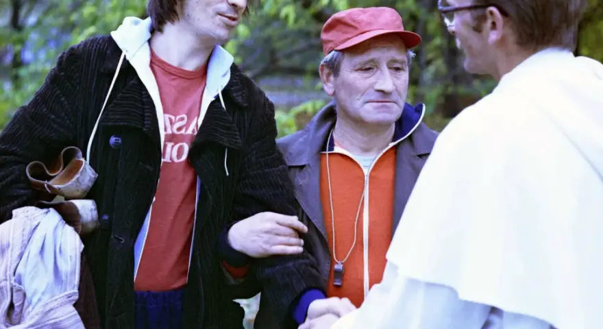 Czesław Nogacki w rozmowie z mężczyzną w białej szacie i z mężczyzną w czerwonej czapce.