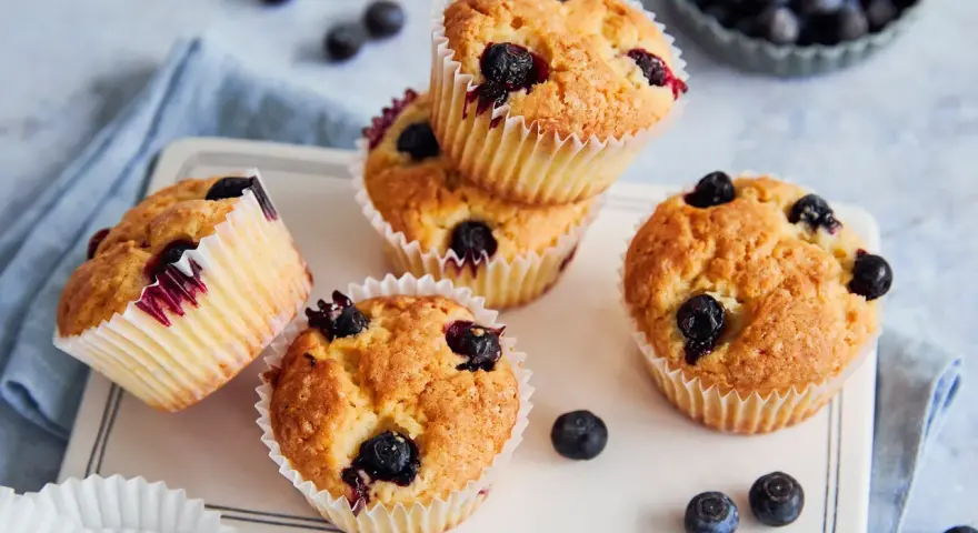 Saftige vegane Blaubeermuffins mit frischen Blaubeeren, auf einem weißen Teller mit blauer Serviette.