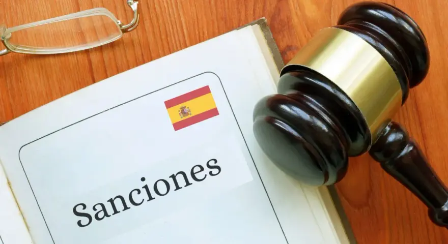 Martillo de juez sobre libro abierto con la palabra "Sanciones" y la bandera de España. Podría ser una multa hacienda.