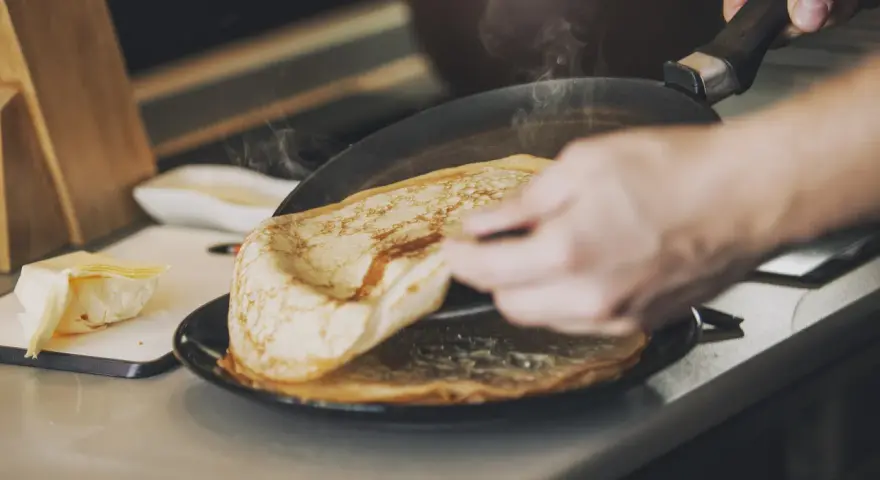 Une main retourne une crêpe dorée dans une poêle fumante. Sur le côté, du beurre frais attend. Ces meilleures crêpes promettent un délice.