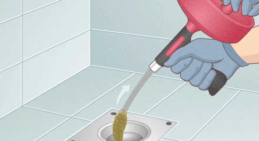 Gloves on, a drain snake is used to clear a clog from a shower drain. This illustrates how to snake a drain.