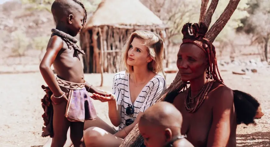 Ludzie Himba w Namibii: młoda kobieta rozmawia z dzieckiem i starszą kobietą w tradycyjnych strojach.