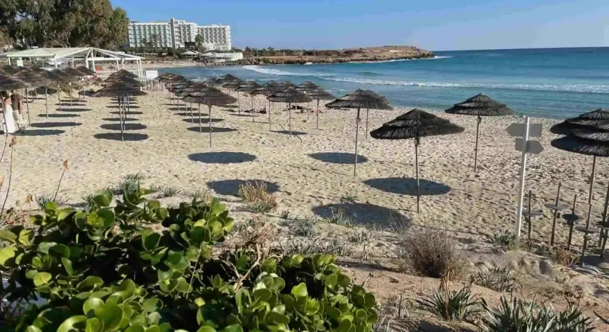 Puste cypr plaże z rzędami parasoli i hotel w tle. Słońce rzuca długie cienie na piasek.