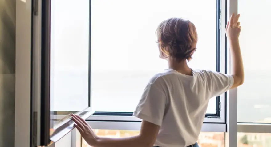 Frau stellt das Fenster ein, um frische Luft hereinzulassen.