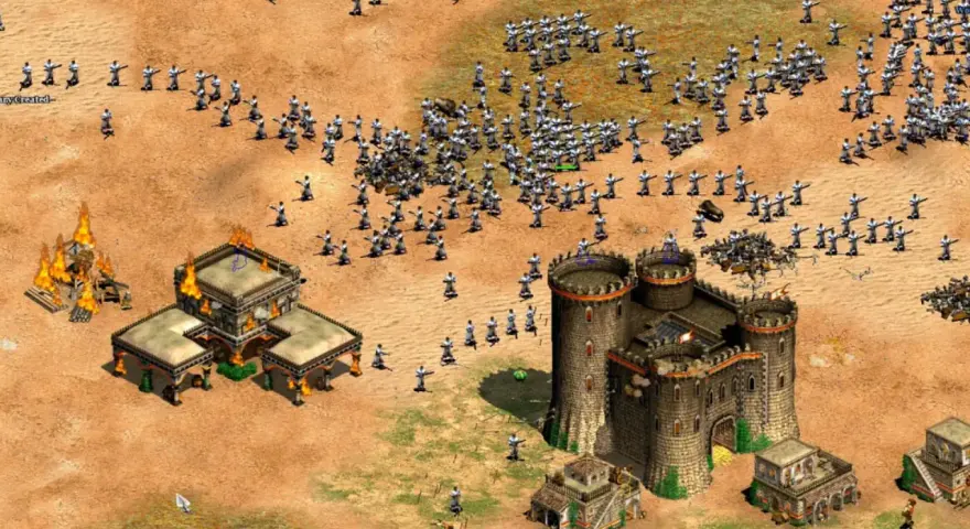 Un ejército avanza en Age of Empires 3, con edificios en llamas y un castillo imponente. ¡Descubre trucos para dominar el campo de batalla!