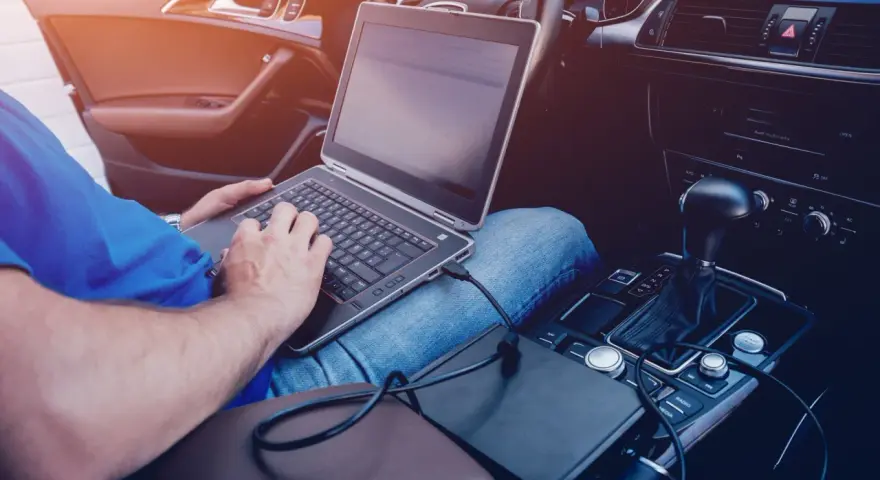 Mężczyzna w samochodzie podłącza laptopa do zasilania, pokazując, jak podłączyć komputer do samochodu.