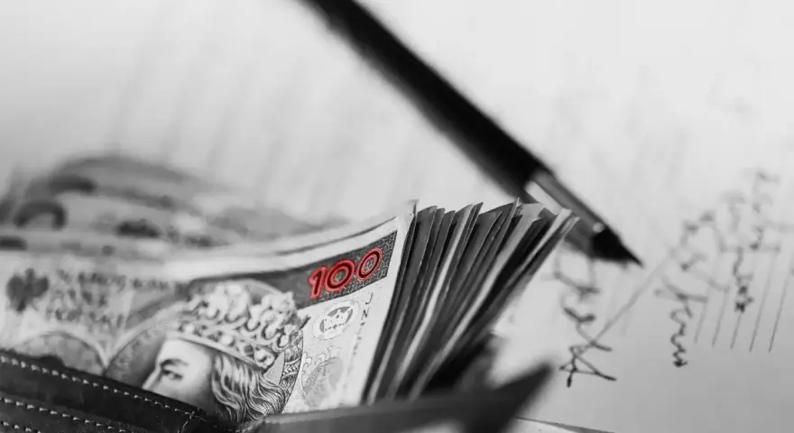 Stos banknotów 100 zł w portfelu, obok długopis i dokumenty. Może to być umowa, gdzie kara umowna jest zapisana.