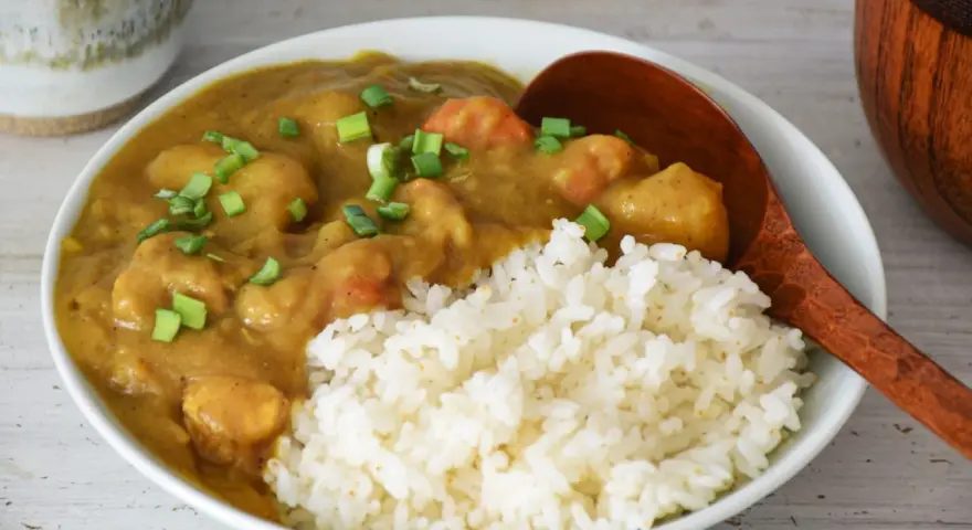 Pyszne japońskie curry z kurczakiem i warzywami, podane z ryżem i posypane szczypiorkiem.