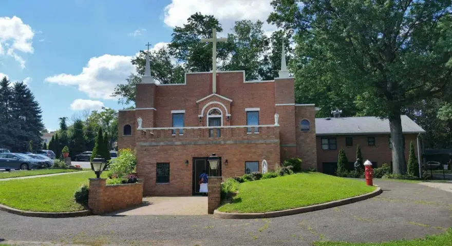 The Holy Face Monastery, a brick building with a large cross, stands on a sunny day.