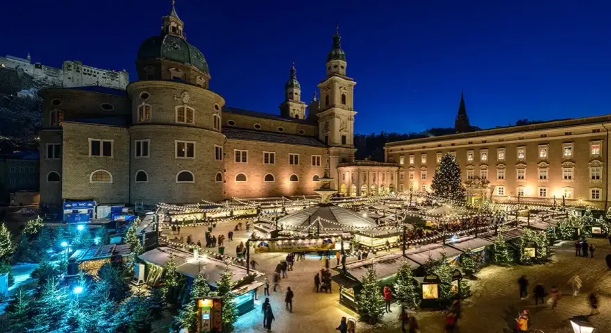 A magical Salzburg Austria Christmas market glows at night, with stalls, trees, and the cathedral creating a festive scene.