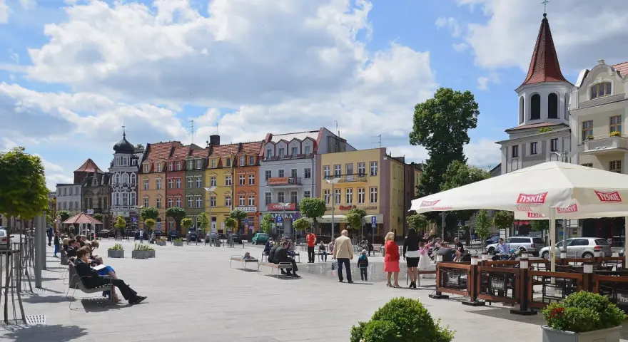 Kolorowy brodnica rynek tętni życiem. Ludzie odpoczywają na ławkach, a kawiarniany ogródek zaprasza do relaksu pod białym parasolem.