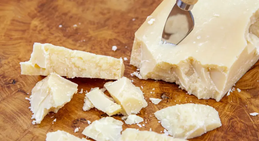 Kawałki Grana Padano na drewnianej desce, gotowe do posypania makaronu lub dodania do sosów.