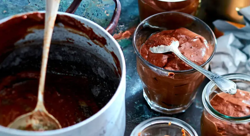 Omas schokoladenpudding mit sahne, cremig und köstlich in Gläsern serviert. Ein Löffel wartet schon.