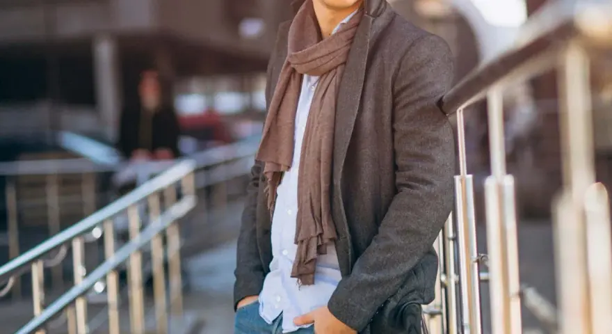 Uomo con cappotto grigio, camicia azzurra e pashmina marrone, un esempio di come indossare una pashmina in modo chic.