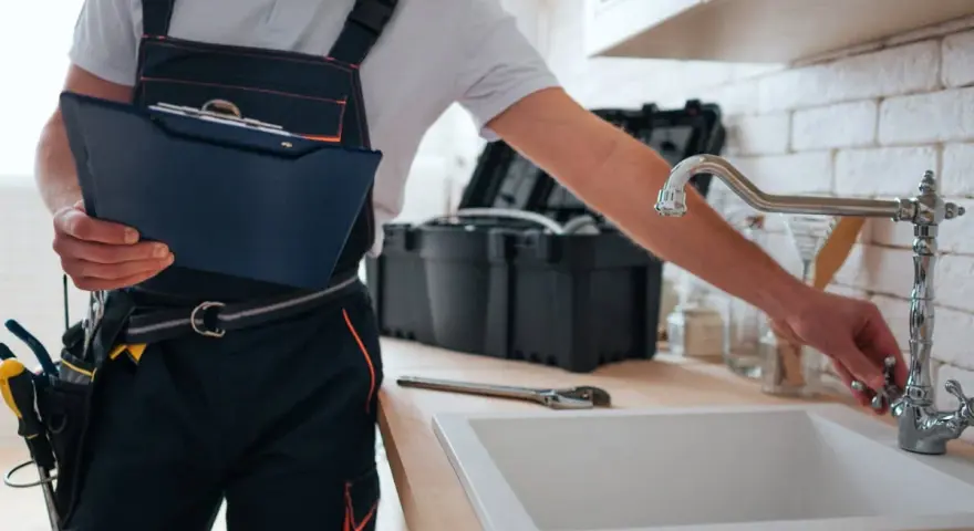 Instrukcja jak zmienić uszczelkę w kranie: hydraulik z narzędziami i teczką przy zlewie.
