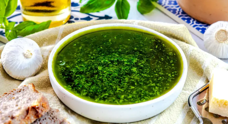 Frisches, grünes Pesto ohne Pinienkerne in einer Schüssel, daneben Knoblauch, Brot und Parmesan.