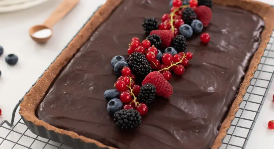 Tarta de chocolate cremosa decorada con frutos rojos frescos: frambuesas, moras, arándanos y grosellas.