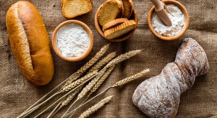 Brot, Getreideähren und Schalen mit Mehl, darunter Vollkornmehl aus Deutschland, liegen auf Jute.