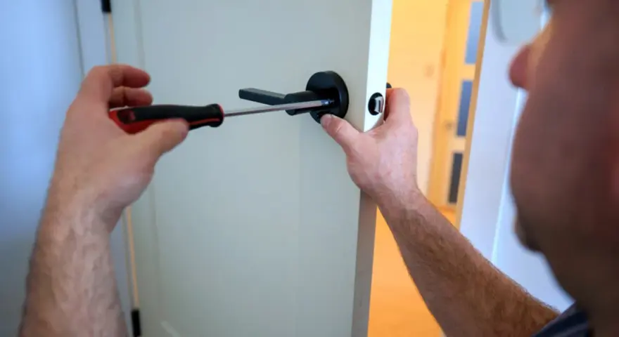 Un homme utilise un tournevis pour changer le ressort de rappel d'une poignée de porte noire.