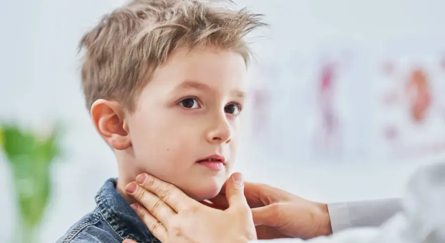 Lekarz bada szyję chłopca, sprawdzając, czy nie ma powiększonych węzłów chłonnych u dzieci. Zdjęcia takie pokazują ważny element diagnostyki.