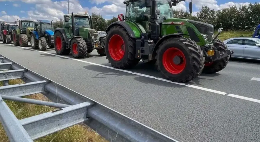 Una fila di trattori attraversa un'autostrada, un'immagine che ricorda che sulle autostrade e strade extraurbane principali è vietata la circolazione di macchine agricole.