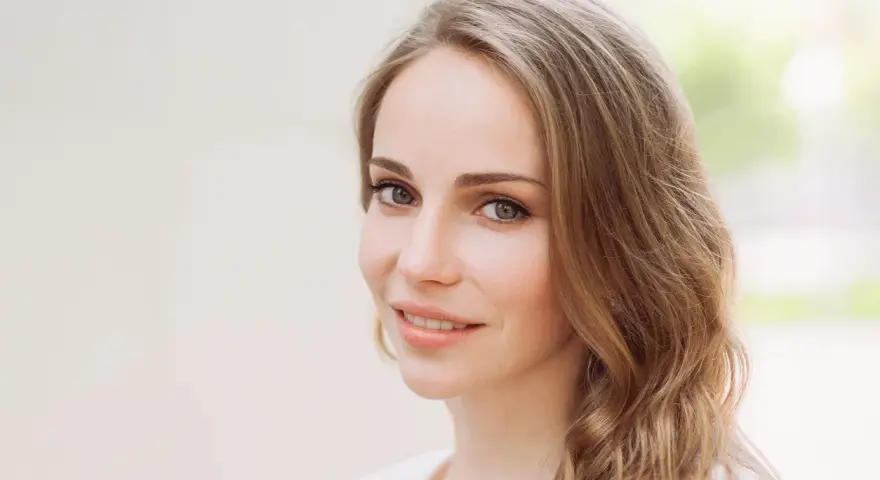 Uśmiechnięta kobieta z mysi blond włosami, delikatnie falującymi na ramionach.
