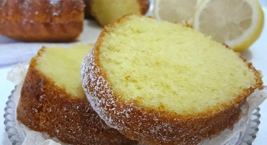 Fette di ciambellone al limone spolverate di zucchero a velo, con fette di limone sullo sfondo.
