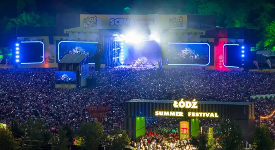 Tłum ludzi na koncercie podczas Łódź Summer Festival 2026. Na scenie gra zespół, a widzowie oświetlają teren telefonami.