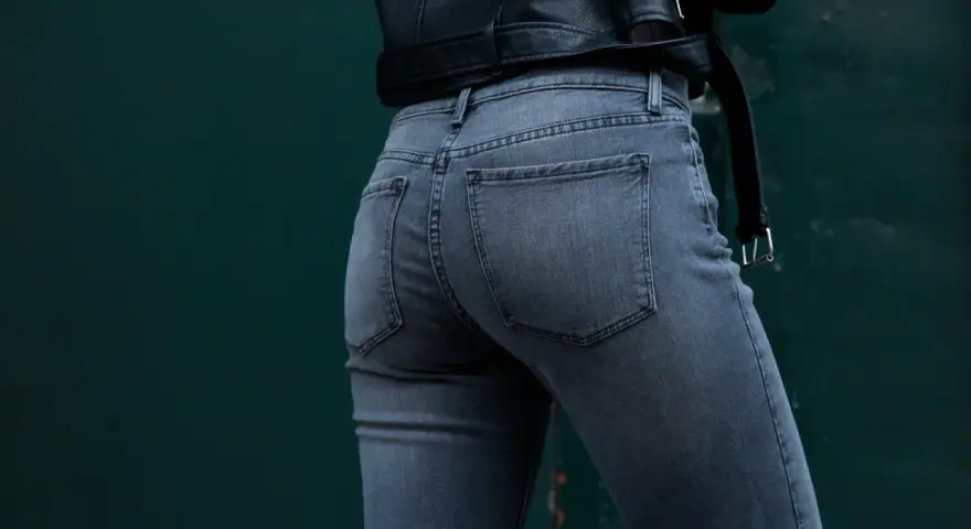 Vue arrière d'une femme portant un jean gris à coupe ajustée, avec une veste en cuir noir.
