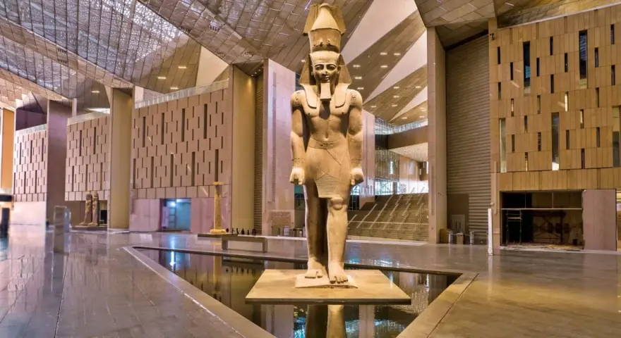 Gigantyczny posąg faraona w holu nowego muzeum w Egipcie, z nowoczesną architekturą i wodnymi elementami.