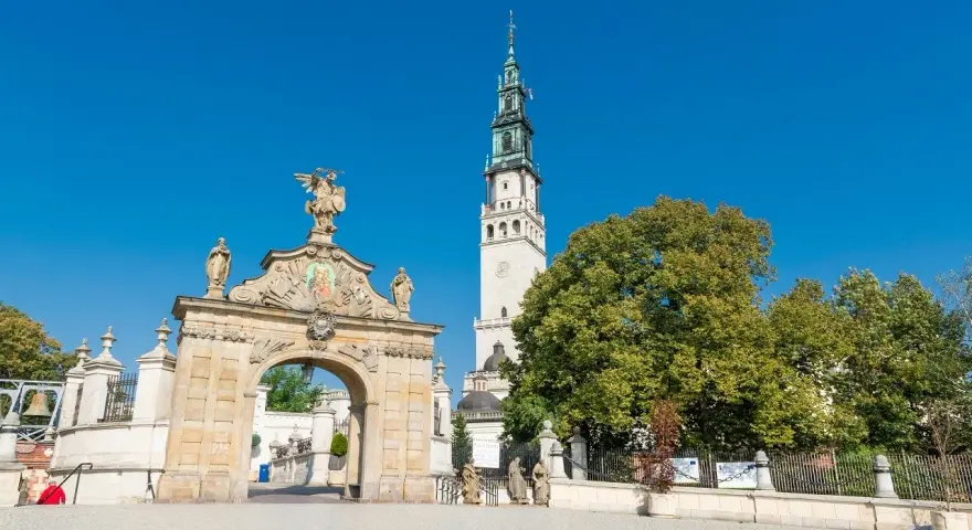 Brama na Jasną Górę, gdzie pielgrzymi zastanawiają się, ile ma lat to miejsce o bogatej historii. Wieża klasztoru góruje nad zielenią.