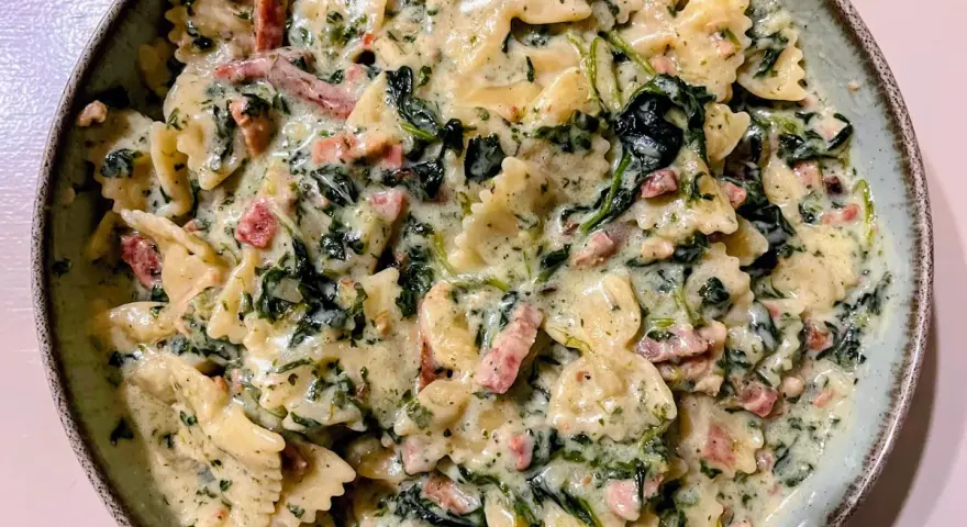 Pyszny makaron farfalle ze szpinakiem i kawałkami boczku w kremowym sosie.