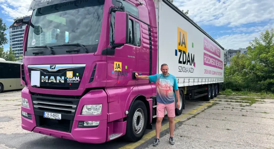 Mężczyzna obok różowej ciężarówki MAN. Na naczepie napis "JA ZDAM SZKOŁA JAZDY". Całkowity koszt prawa jazdy kat C+E jest tu na wyciągnięcie ręki!