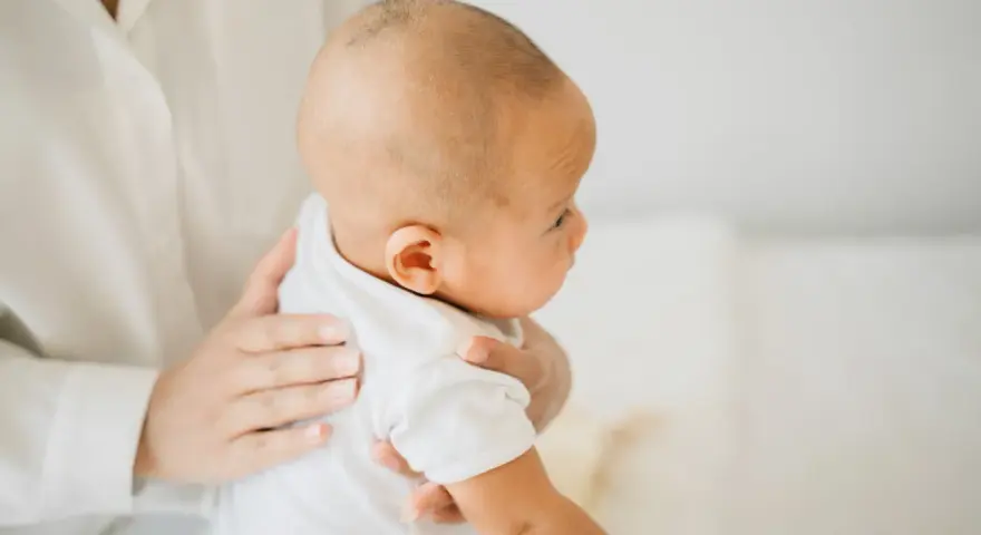 Delikatne odbijanie po jedzeniu. Mama trzyma dziecko, pomagając mu pozbyć się powietrza z brzuszka.