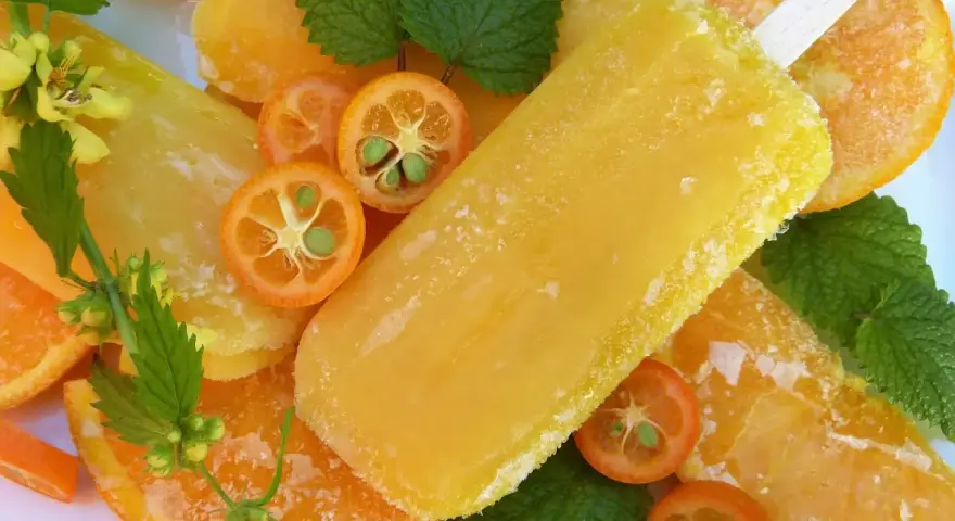 Paletas de helado de naranja, rodajas de naranja y kumquats adornan esta refrescante escena veraniega.