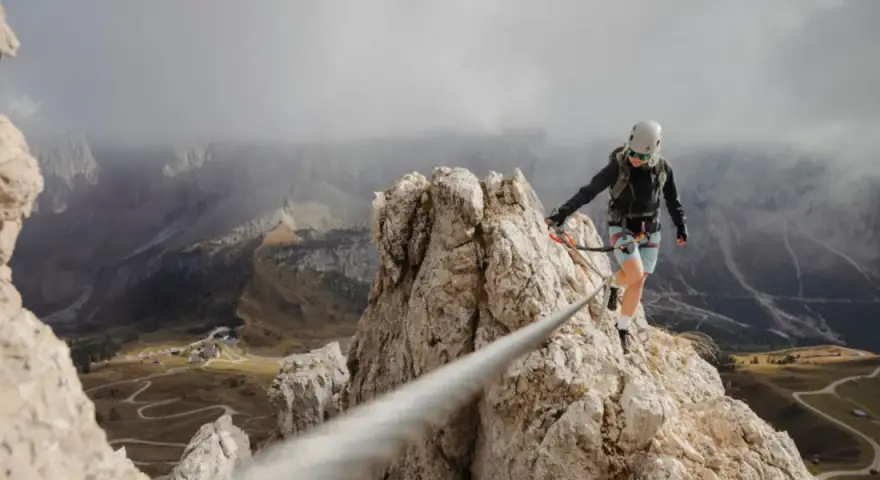Kobieta w kasku i uprzęży pokonuje via ferrata, czyli ubezpieczoną trasę w skałach. Widok zapiera dech w piersiach!