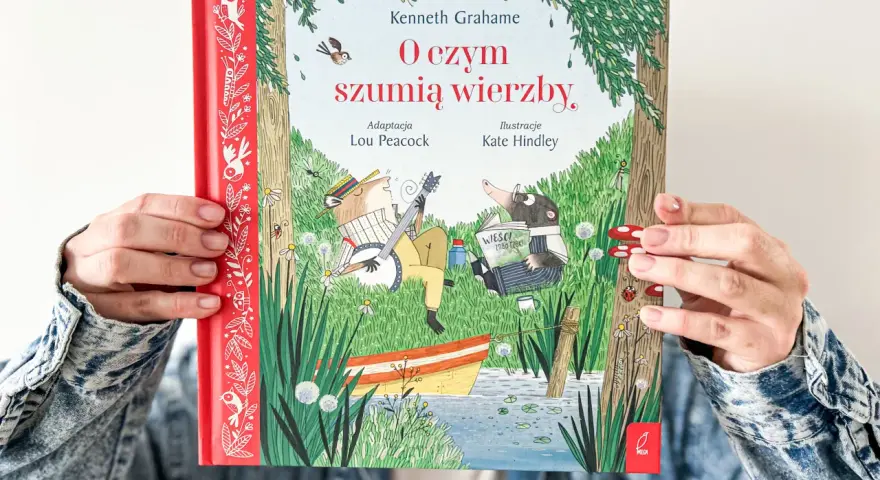 Okładka książki "O czym szumią wierzby" przedstawia zwierzątka nad rzeką. Kret czyta gazetę, a szczur gra na banjo.