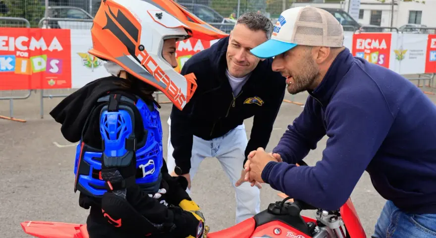 Giovane motociclista donna con casco e protezioni, ascolta i consigli di due uomini.